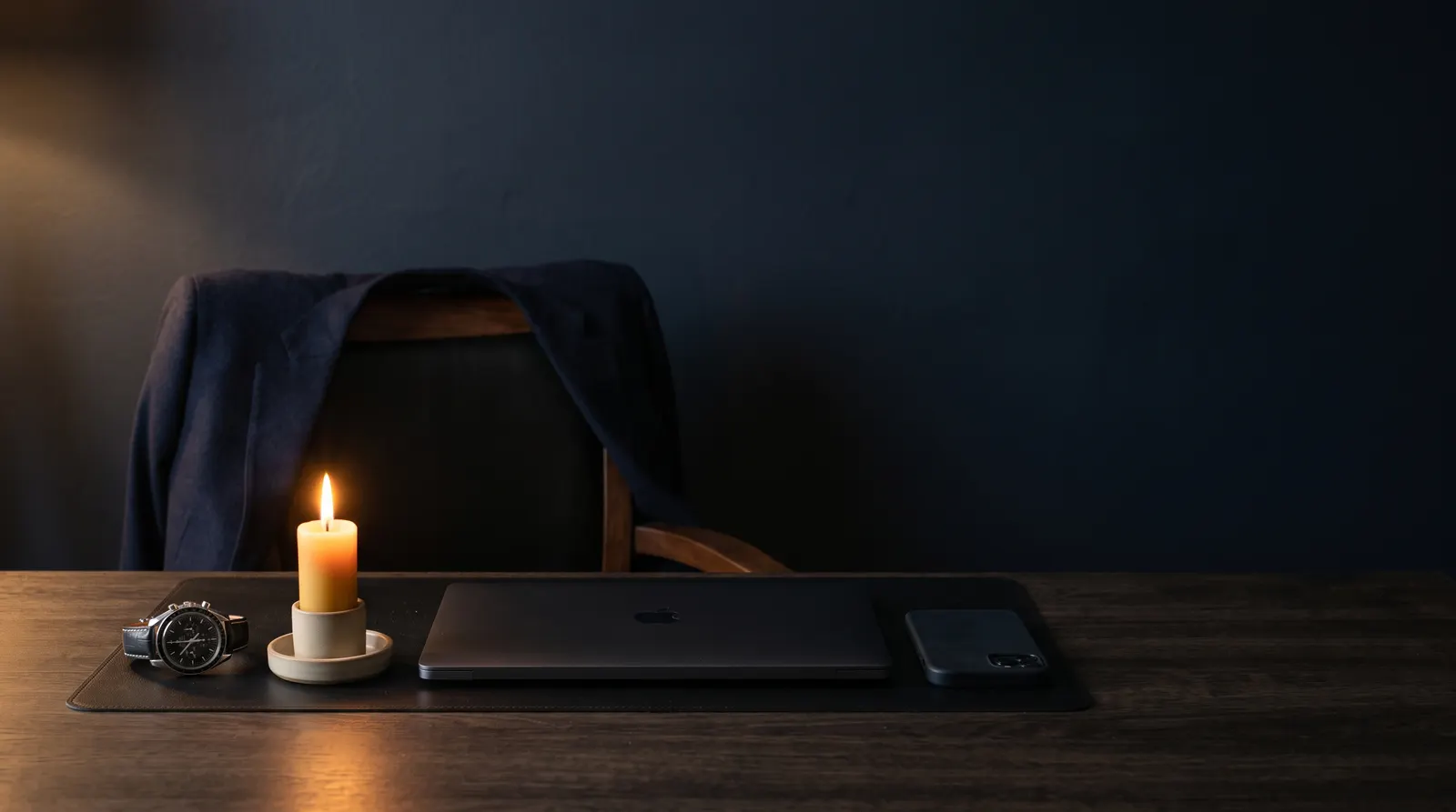 A closed laptop, watch, and candle on a desk at night — a deliberate pause