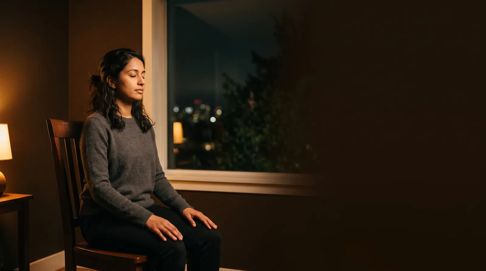 A person meditating in a chair by a window at dusk